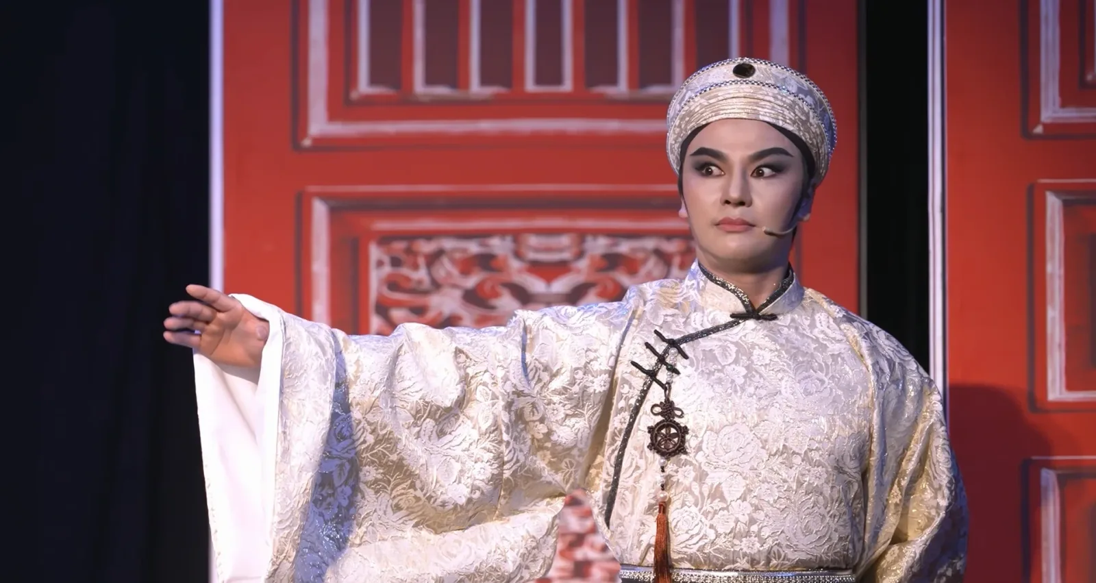 Vua Minh Mạng trong áo gấm trắng đưa tay ban lệnh, ánh mắt liếc ngang đầy toan tính, cảnh “Tùy nghi hành động” trong vở cải lương “Người mang 9 án tử”